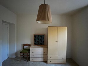 A room with a wooden chair, a cabinet, and a hanging light fixture.