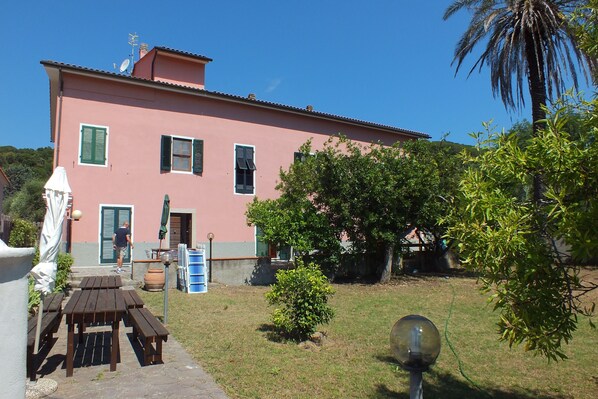 A pink building with a patio area, outdoor furniture, and a small tree.