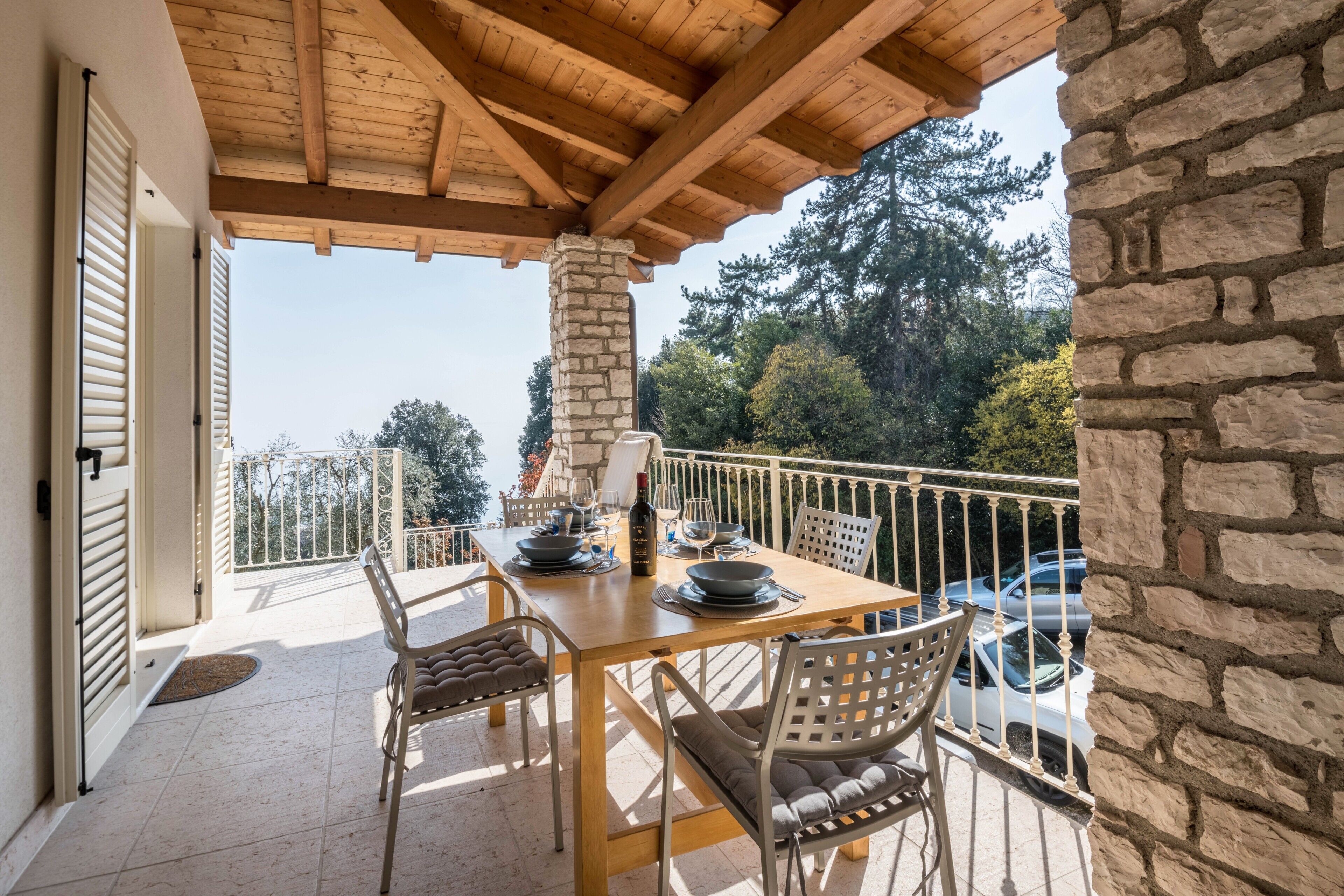 Un balcón de madera con un pilar de piedra, una mesa preparada para comer y vistas de los árboles circundantes.