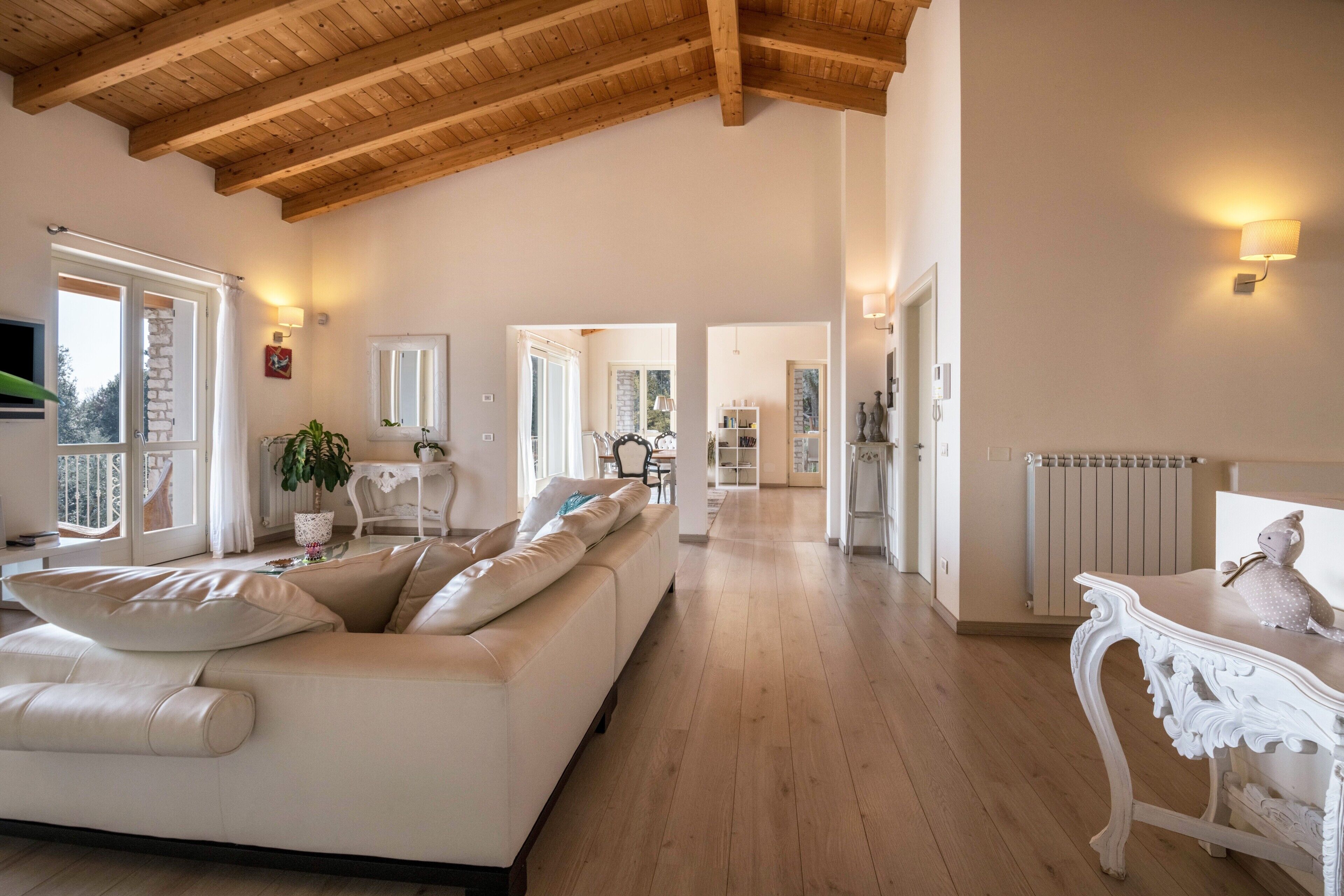 Un vaste salon doté d’un haut plafond en bois, d’un canapé blanc, d’une table blanche et d’une vue dégagée sur l’extérieur grâce à une porte ouverte.