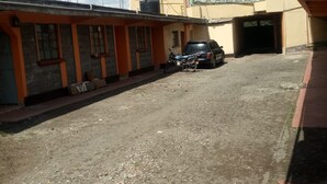 A building with a dirt ground, a parked car, and a motorcycle. - Wanjambi Lodge (Nakuru)