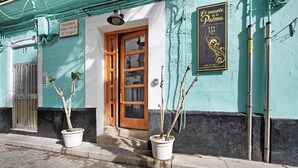 A building with a wooden door, a sign prohibiting playing billiards, and two potted plants on the sidewalk. - Historic and Modern Apartment with Air Conditioning and Wi-Fi (Cádiz)