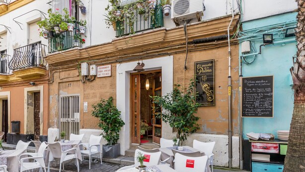 An outdoor café with white tables and chairs, a wooden door entrance, and a chalkboard menu on the wall. - Historic and Modern Apartment with Air Conditioning and Wi-Fi (Cádiz)