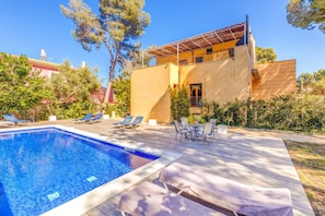 A swimming pool with lounge chairs, a patio area, and a building with a flat roof and large windows.