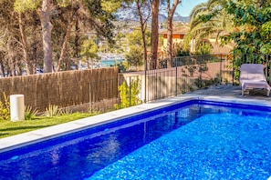 A swimming pool with a wooden deck, a lounge chair, and a view of boats and buildings in the background.