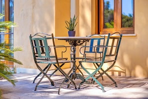 Una mesa con cuatro sillas y una planta en maceta, ubicada en un patio con baldosas y un edificio al fondo.