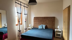 A bedroom with a large bed, a hanging lamp, a bedside table with a lamp, a mirror, and curtains.
