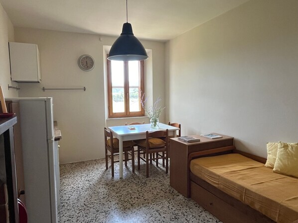 A compact room with a kitchenette, a dining table with chairs, a window with a view, and a bed with a pillow.