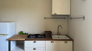 A compact kitchen with a gas stove, a sink, a cabinet, and a clock on the wall.