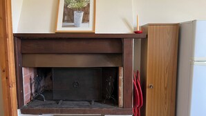 A fireplace with a framed picture above it, a wooden cabinet to the right, and a white refrigerator in the background.