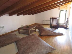 A room with a sloped ceiling, a radiator, a wooden table, and two large cushions.
