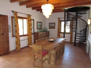 A dining area with a wooden table and chairs, a spiral staircase, and a window with curtains.