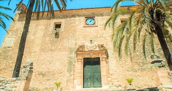 A stone building with a clock, a door, and palm trees.