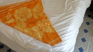 A bed with a white and orange blanket, a red bedspread, and a patterned pillow. - Wasafiri Guest House (Nakuru)