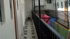 A corridor with a tiled floor, a black metal railing, and a view of a building with a window and a door. - Wasafiri Guest House (Nakuru)