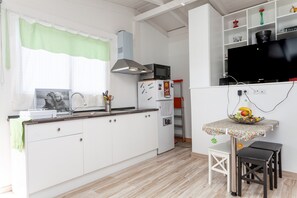 A kitchen with white cabinets, a microwave, a refrigerator, a sink, a dining table with stools, and a television on a stand.