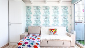 A room with a bed, a sofa, a small table, a wardrobe, and a wall with decorative text. - Holiday Apartment "Atico Casapueblo" Near the Beach with Mountain View (Corralejo)