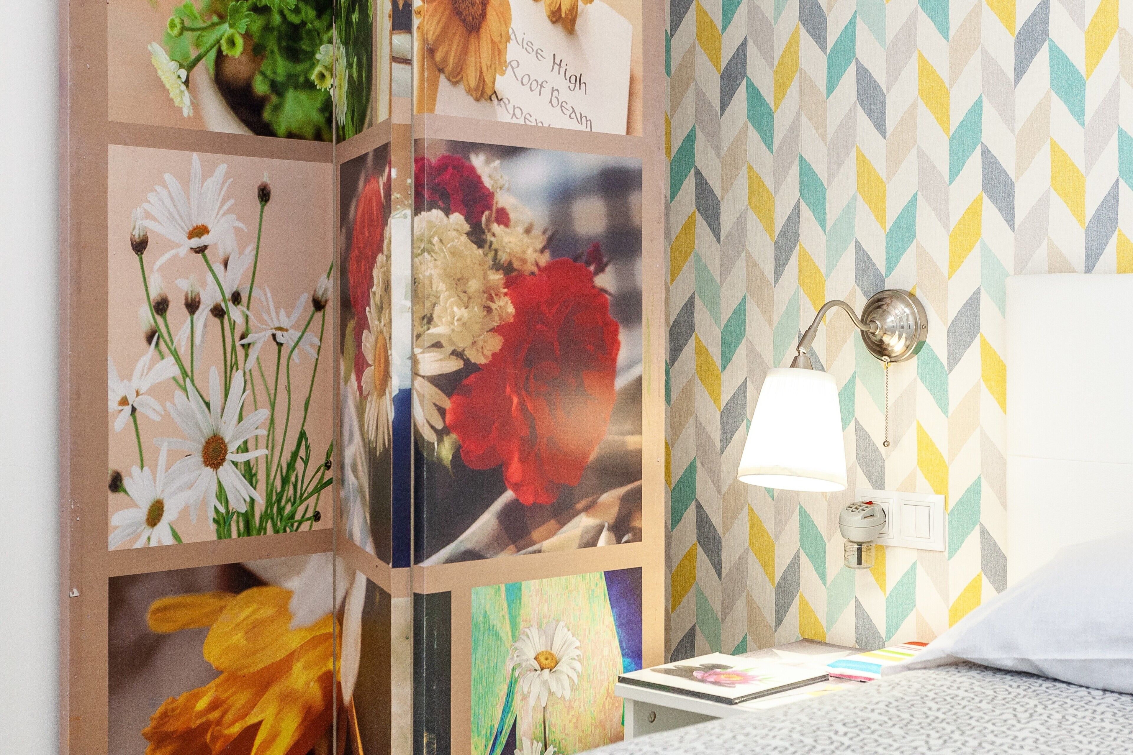 Une chambre avec un lit, une table de chevet avec une lampe et un mur recouvert d’un papier peint à motifs géométriques.