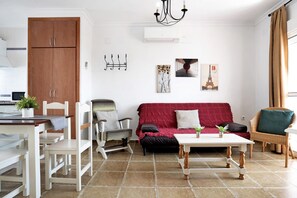 Un salon comprenant un canapé, des fauteuils, une table à manger et un coin cuisine avec des placards.