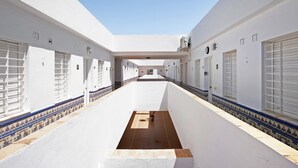 A long corridor with white walls, patterned floor tiles, and a central open space.