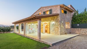 A stone house with a covered patio, a dining area, and a view of the surrounding landscape. - In a Peaceful Location with Garden – Villa Can Ferrer (Alcudia)