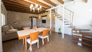 A dining area with a stone wall, wooden ceiling beams, a chandelier, and a staircase. - In a Peaceful Location with Garden – Villa Can Ferrer (Alcudia)