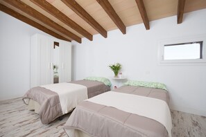 Une chambre avec deux lits, des poutres en bois au plafond, une petite table avec une plante et une fenêtre.