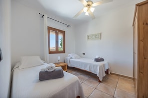 Een hotelkamer met twee bedden, een plafondventilator, een raam met gordijnen en een deur.