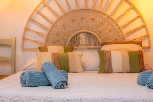 Una cama con toallas enrolladas, un cabecero decorativo y almohadas a rayas.