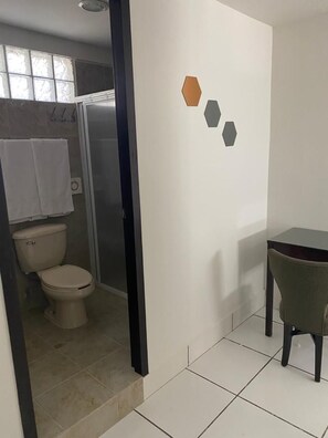 A bathroom with a toilet, shower, and a small table with a chair. - Hotel Suites Fátima (Los Mochis)