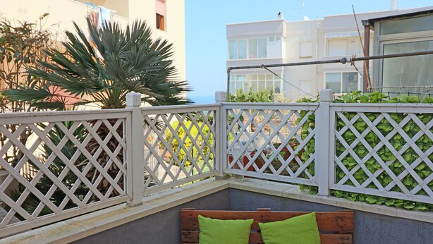 Un balcon avec un banc en bois, une clôture en treillis blanc et une végétation verdoyante.