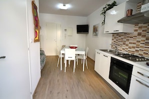 A compact kitchen with white cabinets, a gas stove, a microwave, and a dining area with a table and chairs.