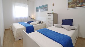 Une chambre avec deux lits, une table de chevet, une commode, un tableau et une fenêtre avec des rideaux.