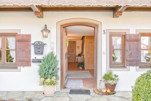 Una entrada de casa con puerta de madera, buzón y plantas en macetas.