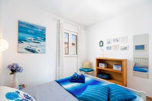 A bedroom with a bed, a wooden shelf, a chair, a window, and a painting on the wall.