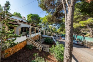 A house with a stone staircase, a balcony, and a view of a road and trees. - Spacious Villa “Casa de Cala Gat” with Sea View, Mountain View, Wi-Fi, Garden & Terrace; Parking Available (Cala Rajada,)
