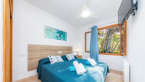Une chambre à coucher avec un lit, une table de chevet, un ventilateur de plafond, une fenêtre avec des rideaux et un tableau au mur.