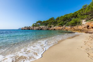 A beach with clear water, sandy shore, and rocky cliffs with trees. - Spacious Villa “Casa de Cala Gat” with Sea View, Mountain View, Wi-Fi, Garden & Terrace; Parking Available (Cala Rajada,)