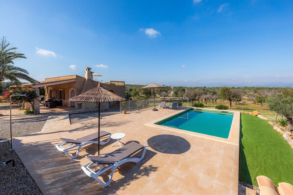 A pool area with lounge chairs, a barbecue, and a view of the landscape.