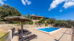 Un área de piscina con sillones de descanso, una sombrilla de paja y un muro de piedra.