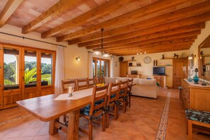 Un comedor con mobiliario de madera, un televisor y una cocina con armarios de madera.