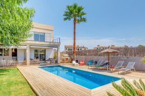 A swimming pool with lounge chairs, a palm tree, and a house with a balcony. - Beautiful Villa Ronda Estación with Pool, Terrace, Garden, Wi-Fi & Air Conditioning; Street Parking Available (Porreras)