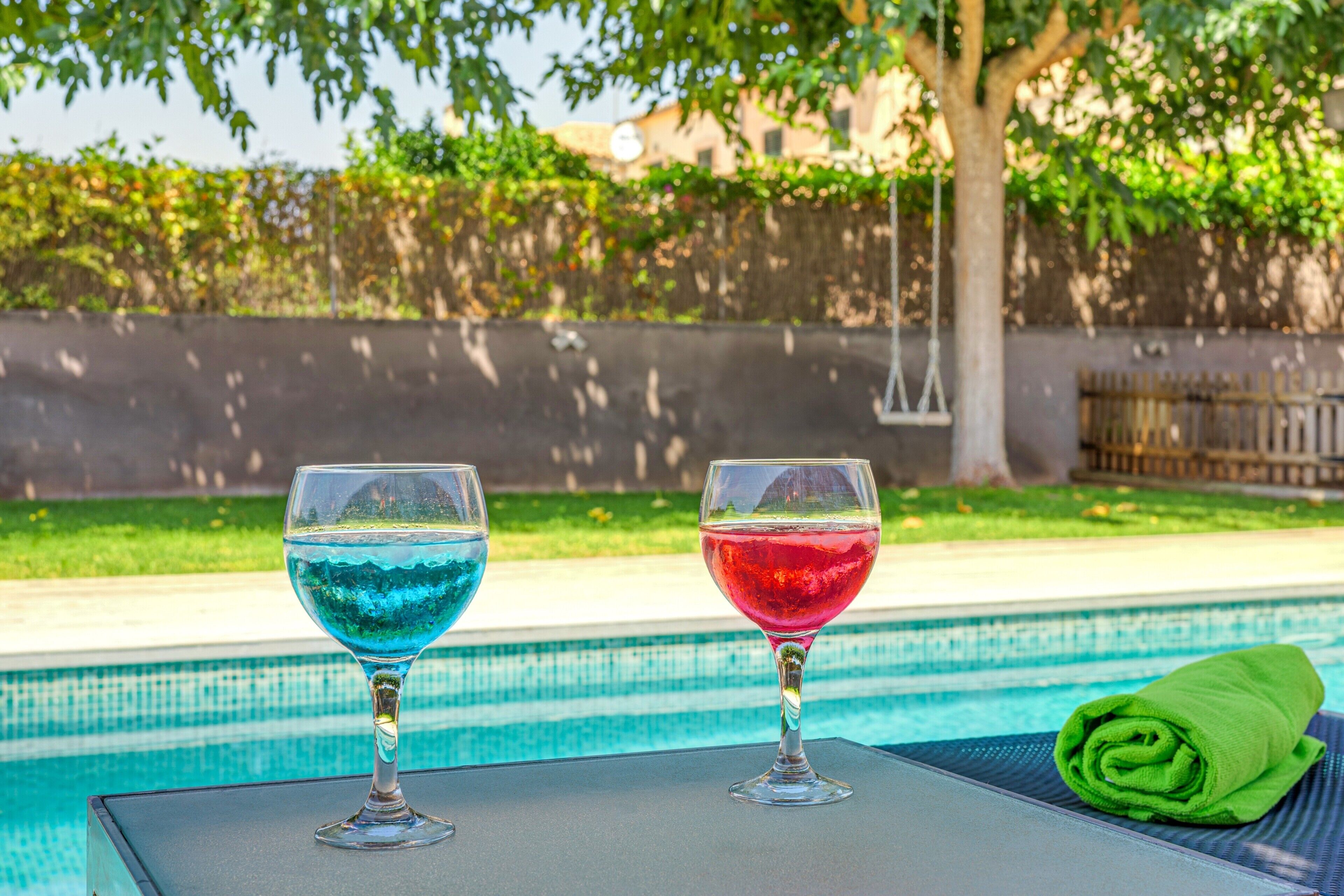 Two glasses of colored liquid on a table by a pool.