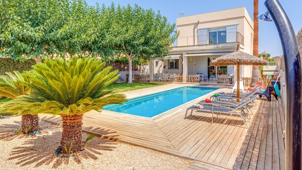 Een modern huis met een zwembad, een terras en een palmboom.
