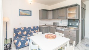 A compact kitchen with a dining table, chairs, a sofa, and a small island with a stove.