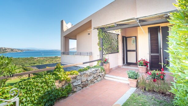 A modern house with a stone wall, potted plants, and a view of the sea.