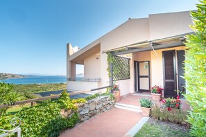 A modern house with a stone wall, potted plants, and a view of the sea.