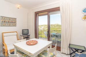 Ein Zimmer mit Esstisch, Stühlen, Fernseher und einem Balkon mit Blick.