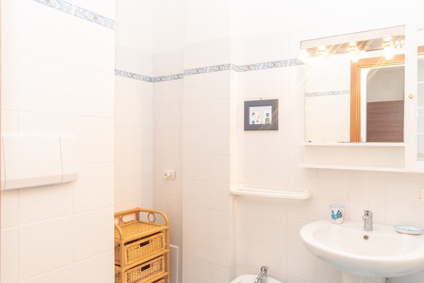 A bathroom with white tiled walls, a white sink, a mirror, and a wicker basket.
