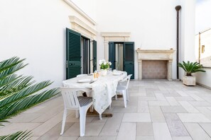 A patio with a table set for dining, green shutters, a fireplace, and potted plants. - Casa Vacanza Pizzicchia (Muro Leccese)